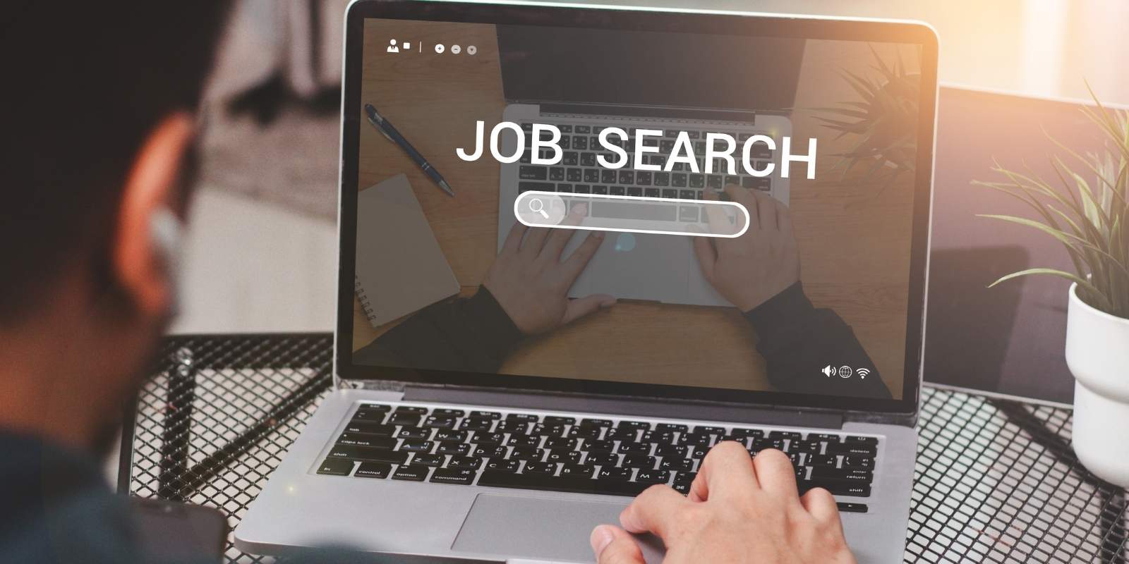Over-the-shoulder view of a person using a laptop with "JOB SEARCH" and a search bar displayed on the screen, representing a job seeker searching for a remote job online.